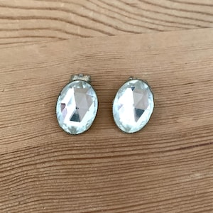 Puede incluir: Un par de pendientes de cristal transparente de forma ovalada con engastes plateados.