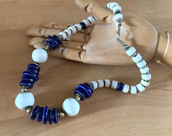 May include: A white and blue ceramic bead necklace with a silver clasp. The necklace features alternating white and blue round beads, with some of the blue beads being stacked.