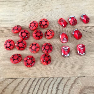 May include: A collection of red and silver buttons with intricate designs. The red buttons are round and have a black and white pattern. The silver buttons are various shapes and have a silver and red pattern.