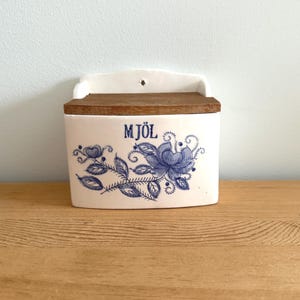 Caja de harina vintage azul y blanca con tapa de madera, tarro de cerámica con decoración de paja azul cobalto.