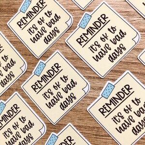 Puede incluir: Un conjunto de seis pegatinas de recordatorio amarillas con acentos de cinta azul. Cada pegatina dice "REMINDER it's ok to have bad days".