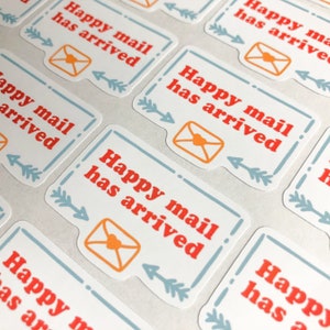 May include: A set of white stickers with blue borders and red text that says "Happy mail has arrived". Each sticker features a small orange envelope with a red heart.