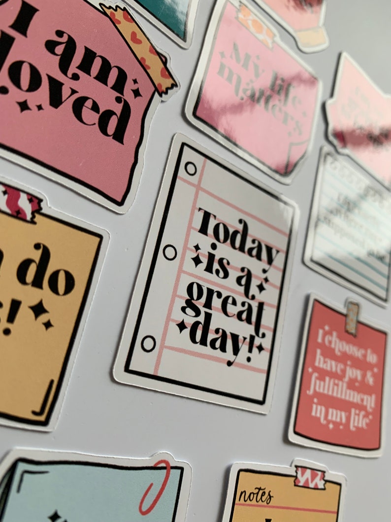 K&ouml;nnte beinhalten: Ein Set bunter Sticker mit positiven Affirmationen. Die Sticker zeigen S&auml;tze wie "Ich bin geliebt", "Mein Leben z&auml;hlt", "Heute ist ein gro&szlig;artiger Tag!" und "Ich w&auml;hle Freude und Erf&uuml;llung in meinem Leben".