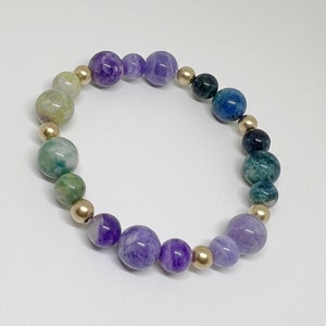 May include: A multi-colored gemstone bracelet with purple, green, and blue beads separated by gold beads.