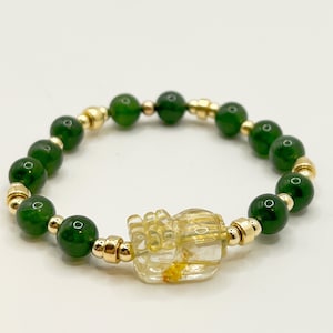 Könnte beinhalten: Ein Armband aus grünem Jade und goldenen Perlen mit einem Anhänger aus klarem Quarz. Der Anhänger ist mit einem detaillierten Design verziert.
