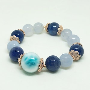 May include: A blue and white gemstone bracelet with gold accents. The bracelet features a large, round, white gemstone with blue swirls, surrounded by smaller blue and white gemstones.