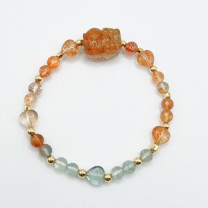 May include: A gold bracelet with orange and green heart-shaped beads and a carved orange stone charm.