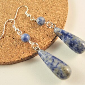 May include: A pair of silver dangle earrings with blue teardrop-shaped stones. The stones have a marbled pattern.