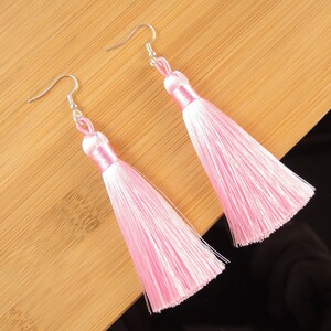 May include: A pair of pink tassel earrings with silver hooks. The tassels are made of soft, silky threads and hang down about 7.5 cm.