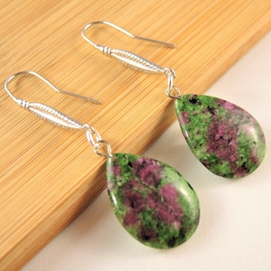 Puede incluir: Pendientes colgantes con piedras preciosas en forma de lágrima, verdes y magenta. Los pendientes tienen ganchos decorativos plateados. Las piedras miden aproximadamente 2,5 cm de largo.