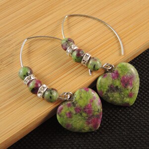 May include: A pair of silver hoop earrings with green and pink gemstone beads and heart-shaped pendants.