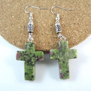 May include: Earrings with green and red cross pendants. The crosses are made of speckled stone and hang from silver-coloured hooks with decorative beads. The earrings are a religious item.