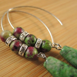 Peut inclure: Une paire de boucles d'oreilles cr&eacute;oles en argent avec des perles de pierres pr&eacute;cieuses vertes et roses et des entretoises argent&eacute;es. Les perles sont rondes et ont un aspect marbr&eacute;.
