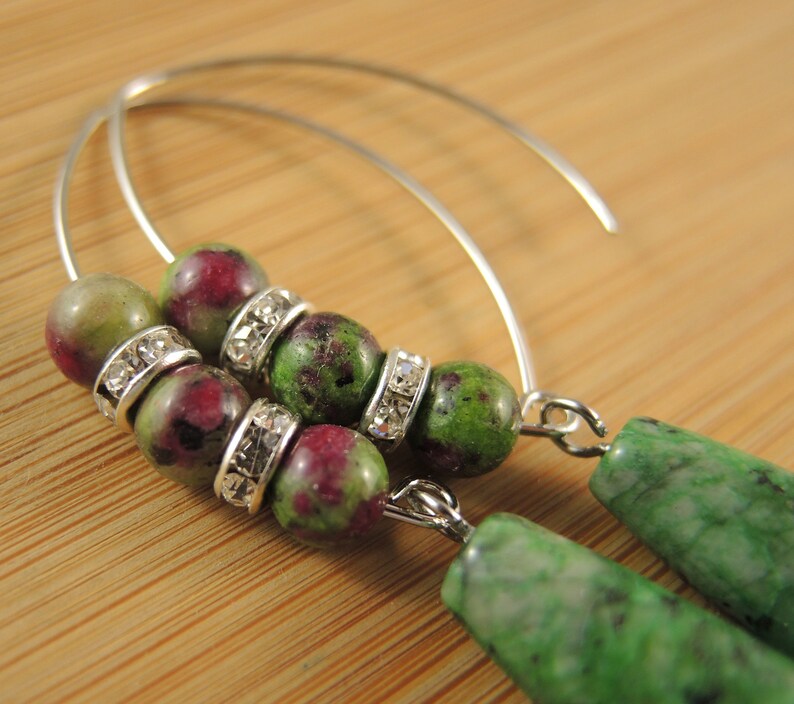 Peut inclure: Une paire de boucles d'oreilles cr&eacute;oles en argent avec des perles de pierres pr&eacute;cieuses vertes et roses et des entretoises argent&eacute;es. Les perles sont rondes et ont un aspect marbr&eacute;.