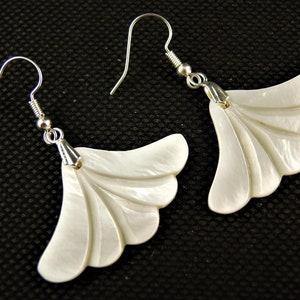 May include: A pair of white shell earrings with a fan-shaped design. The earrings are made of mother of pearl and have silver hooks.