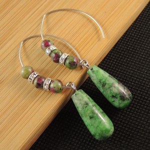 May include: A pair of silver hoop earrings with green and pink gemstone beads and a teardrop-shaped green gemstone pendant.