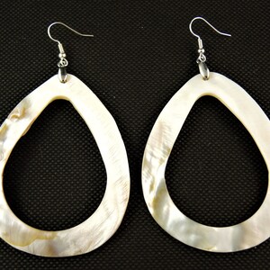 May include: A pair of large, pear-shaped earrings. The earrings are made of a light-coloured, iridescent material, possibly mother-of-pearl, with a silver-coloured hook. The teardrop-shaped earrings have a hollow centre and a smooth, polished surface.
