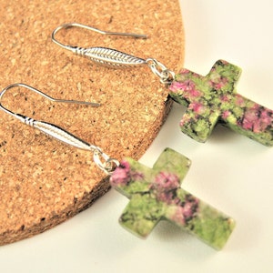 May include: A pair of silver earrings with green and pink cross-shaped pendants. The crosses are made of a speckled stone with green and pink hues.