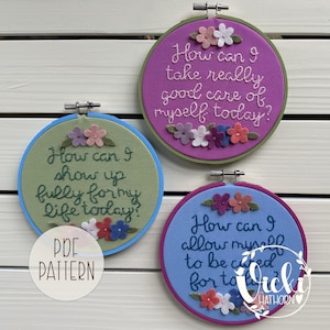 Peut inclure: Trois cerceaux brodés avec des citations inspirantes. Le cerceau supérieur est violet avec le texte "How can I take really good care of myself today?" et des motifs floraux. Les autres cerceaux ont des motifs et du texte similaires.