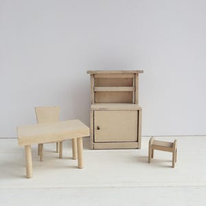 May include: A set of miniature wooden furniture in a light beige color. The set includes a table with two chairs, a cabinet with shelves and a small stool.