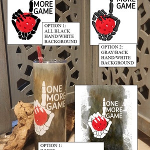 Può includere: Un bicchiere bianco con un'immagine in bianco e nero di una mano scheletrica che tiene una palla da pickleball rossa. Il testo "One More Game" è stampato sul bicchiere. Il bicchiere è su una superficie di legno.