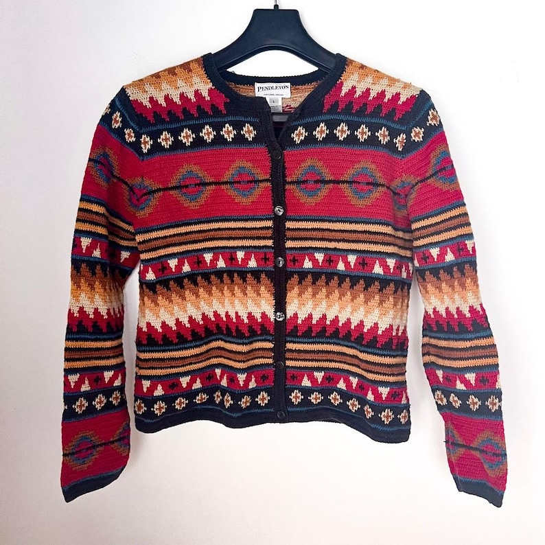 May include: A button-up cardigan sweater with a Southwestern geometric pattern in red, black, tan, and blue. The sweater has long sleeves and a black collar. The brand name "Pendleton" is visible on the label.
