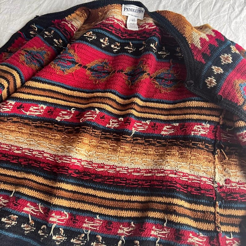 May include: A Pendleton cardigan in a vibrant mix of colors, including red, black, tan, and blue. The open cardigan features a button closure and a detailed, patterned design. The label is visible at the top.