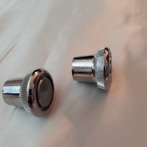 May include: Two silver metal knobs with a textured surface. The knobs have a round top and a cylindrical base.