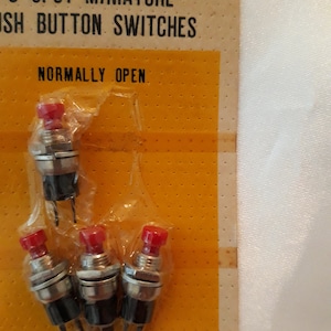 May include: A package of five red push button switches labeled "5 SPST Miniature Push Button Switches" and "Normally Open". The switches are packaged in clear plastic and are on a yellow card with black polka dots. The card also says "Tom Med. In Japan for Radio Shack."