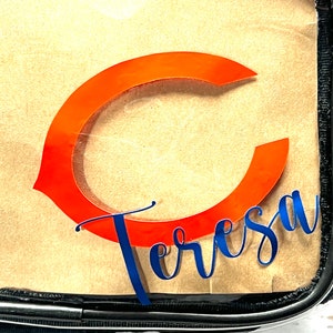 May include: Clear plastic cosmetic bag with a large orange "C" and the name "Teresa" written in blue cursive.