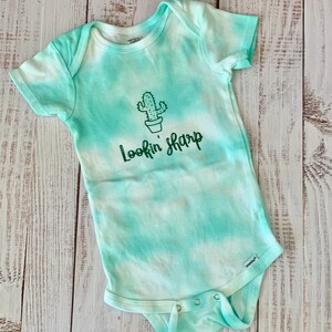 May include: A green and white tie-dye baby onesie with a green cactus and the text "Lookin' Sharp" in green.