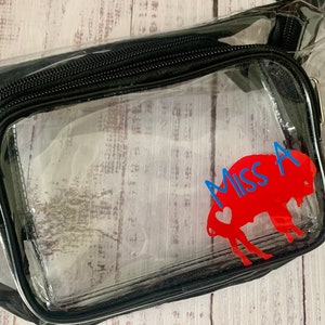 May include: Clear plastic fanny pack with a black zipper and a red buffalo silhouette with a blue heart and the text "Miss A" on it.