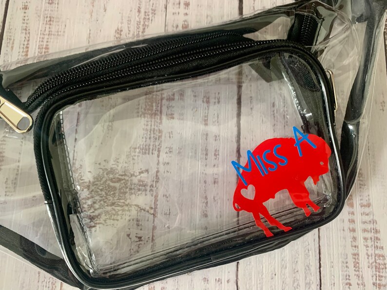 May include: Clear plastic fanny pack with a black zipper and a red buffalo silhouette with a blue heart and the text "Miss A" on it.