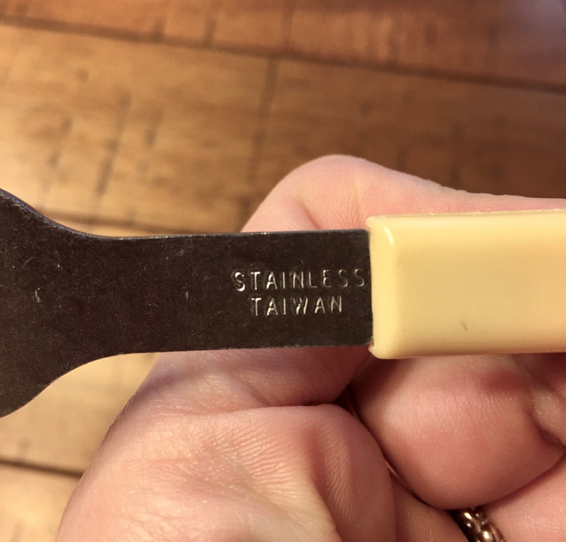 Op de afbeelding: Een close-up van een metalen bestek met een cr&egrave;mekleurige handgreep. Het bestek is gemarkeerd met "Stainless Taiwan".