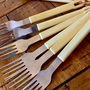 Op de afbeelding: Een set van zes vintage vorken met ivoor gekleurde kunststof handvatten. De vorken zijn gemaakt van roestvrij staal en hebben een klassiek ontwerp.