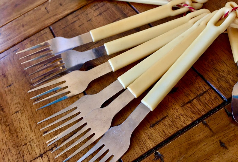 Op de afbeelding: Een set van zes vintage vorken met ivoor gekleurde kunststof handvatten. De vorken zijn gemaakt van roestvrij staal en hebben een klassiek ontwerp.