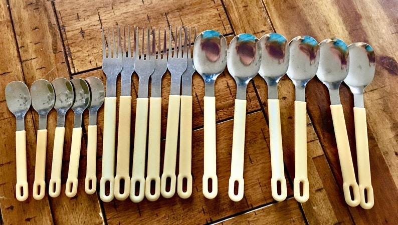 Op de afbeelding: Een set van 18 zilverkleurige bestekdelen met cr&egrave;mekleurige handvatten. De set bevat vorken en lepels.