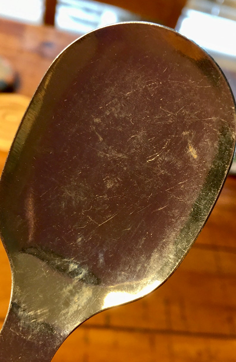 Op de afbeelding: Een close-up van een zilveren lepel met een glanzend oppervlak en zichtbare krassen. De lepel is licht gebogen en heeft een afgeronde kom.