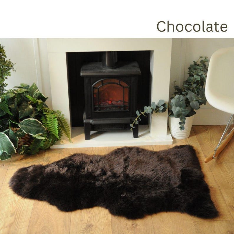 May include: A brown faux fur rug with a shaggy texture. The rug is laid out on a wooden floor in front of a fireplace.