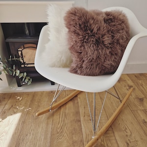 May include: A white rocking chair with a white and brown fluffy pillow. The chair has a white seat, metal legs, and wooden rockers. The pillows are a soft, textured material.