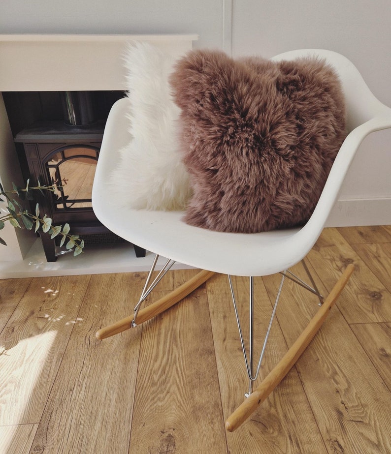 May include: A white rocking chair with a white and brown fluffy pillow. The chair has a white seat, metal legs, and wooden rockers. The pillows are a soft, textured material.