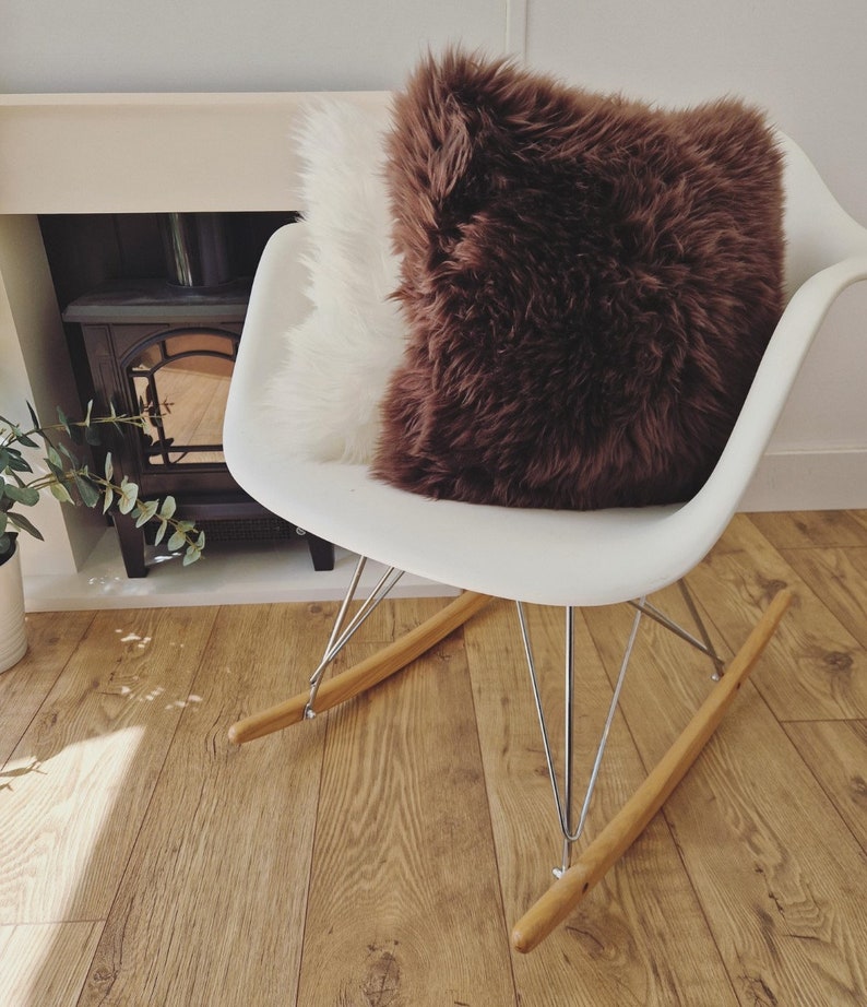 May include: A white rocking chair with a brown and white fluffy pillow. The chair has a white seat, metal legs, and wooden rockers. The pillows have a shaggy texture, adding a cozy element to the room.