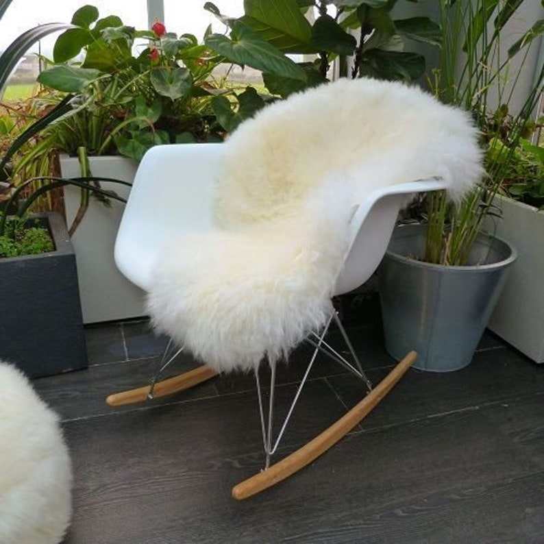 May include: A white sheepskin rug placed on a white rocking chair with wooden arms and chrome legs. The chair is in a room with plants in pots.