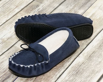May include: A pair of blue suede moccasins with a white fuzzy lining. The moccasins have a decorative fringe around the opening and a black rubber sole.