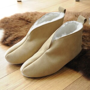 May include: A pair of beige suede slippers with a white fleece lining. The slippers have a pointed toe and a low heel.