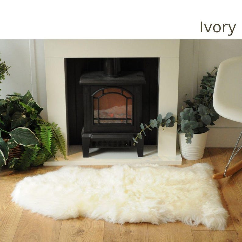 May include: A white sheepskin rug in front of a fireplace with a black fireplace insert. The rug is ivory in color and has a fluffy texture. The fireplace is made of brick and has a black metal insert. The insert has a glass door and a glowing fire inside.