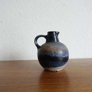 Könnte beinhalten: Kleine, runde Keramikkrug mit Henkel. Der Krug hat eine dunkelblaue Glasur oben und unten, mit einem schwarzen und einem braunen Band in der Mitte. Er steht auf einer Holzoberfläche.