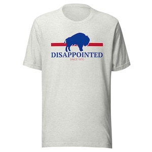 Könnte beinhalten: Ein hellgrau meliertes Kurzarm-T-Shirt mit einer blauen Büffelsilhouette über einem horizontalen roten Strich. Unter dem Strich steht der Text DISAPPOINTED in blauen Großbuchstaben, darunter der rote Text SINCE 1970.