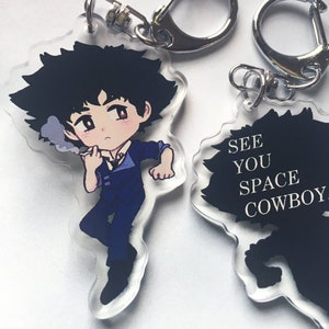 Puede incluir: Un llavero de acrílico transparente con una ilustración de dibujos animados de Spike Spiegel de la serie de anime Cowboy Bebop. El llavero tiene un anillo de metal plateado y una silueta negra de Spike con el texto "See You Space Cowboy" en la parte posterior.