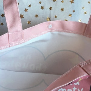 May include: Pink canvas tote bag with a white interior and a heart design. The bag has a button closure and the text "not empty" printed on the front.